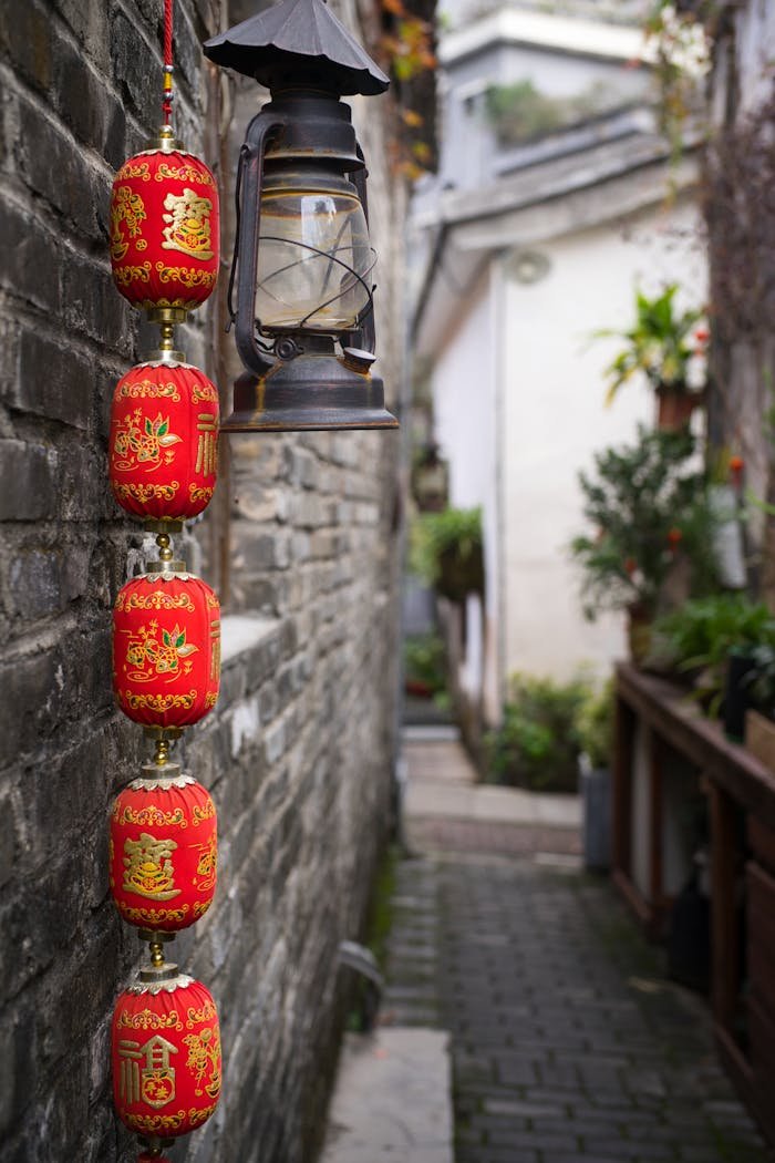 gallery-2 Vibrant red Chinese lanterns hanging next to a vintage lamp in a narrow stone alley.