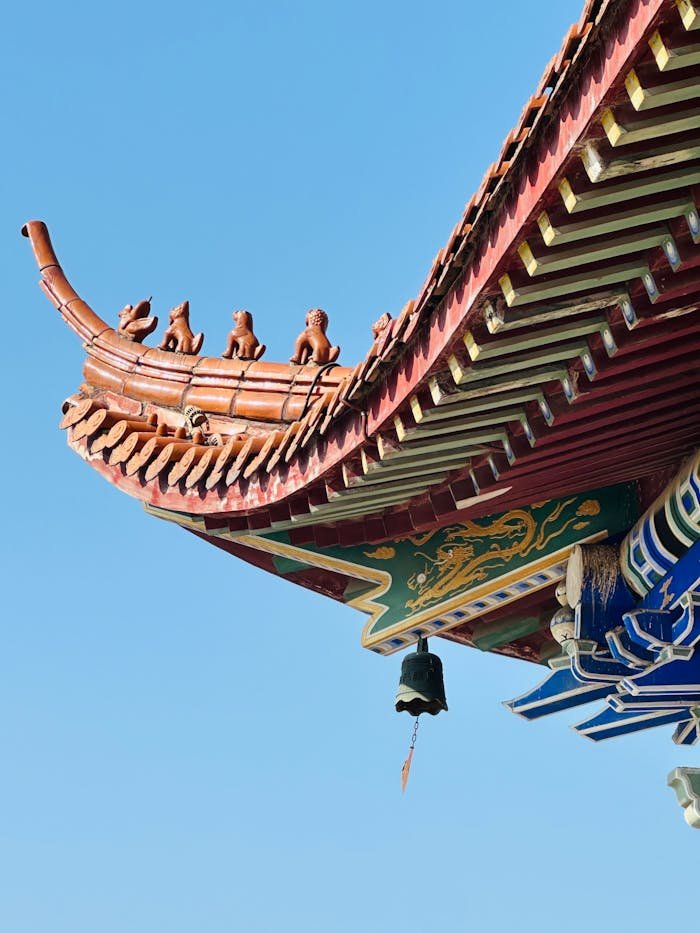 gallery-5 A decorative traditional Chinese temple roof with ornate figures against a clear blue sky.