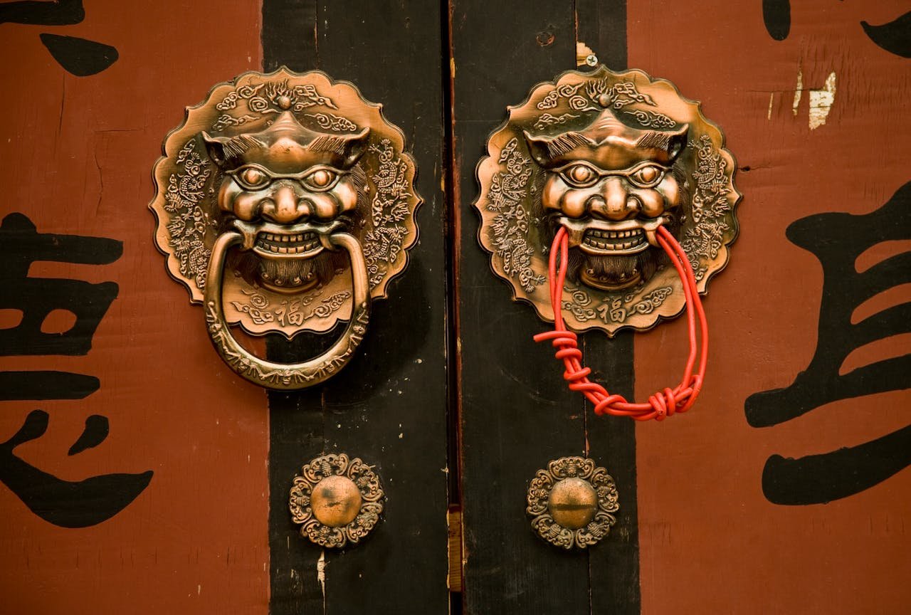 about-img Close-up of ornate brass door handles with intricate designs on a traditional Chinese wooden door.